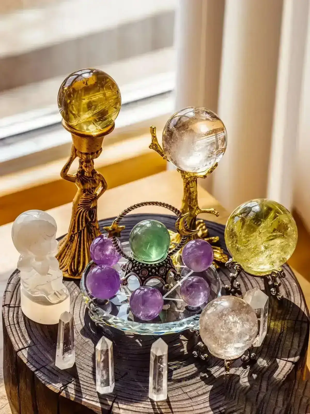 AuraCharming yellow citrine sphere on golden tree stand, green aventurine tower, amethyst cluster on wood disc, clear quartz figurine in sunlight by window