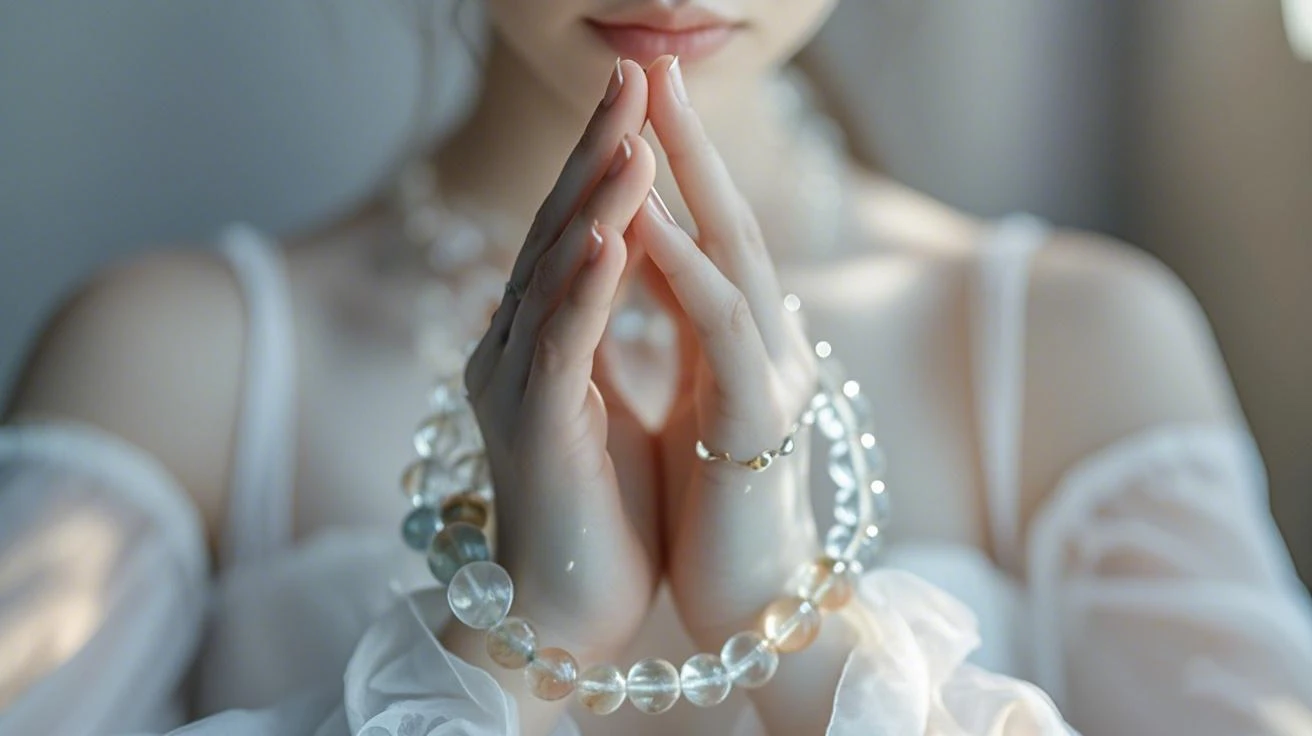 Auracharming Young woman in white dress meditating with crystal jewelry, hands pressed together in prayer position. Spiritual guidance on wearing crystals on left or right hand for chakra balancing.
